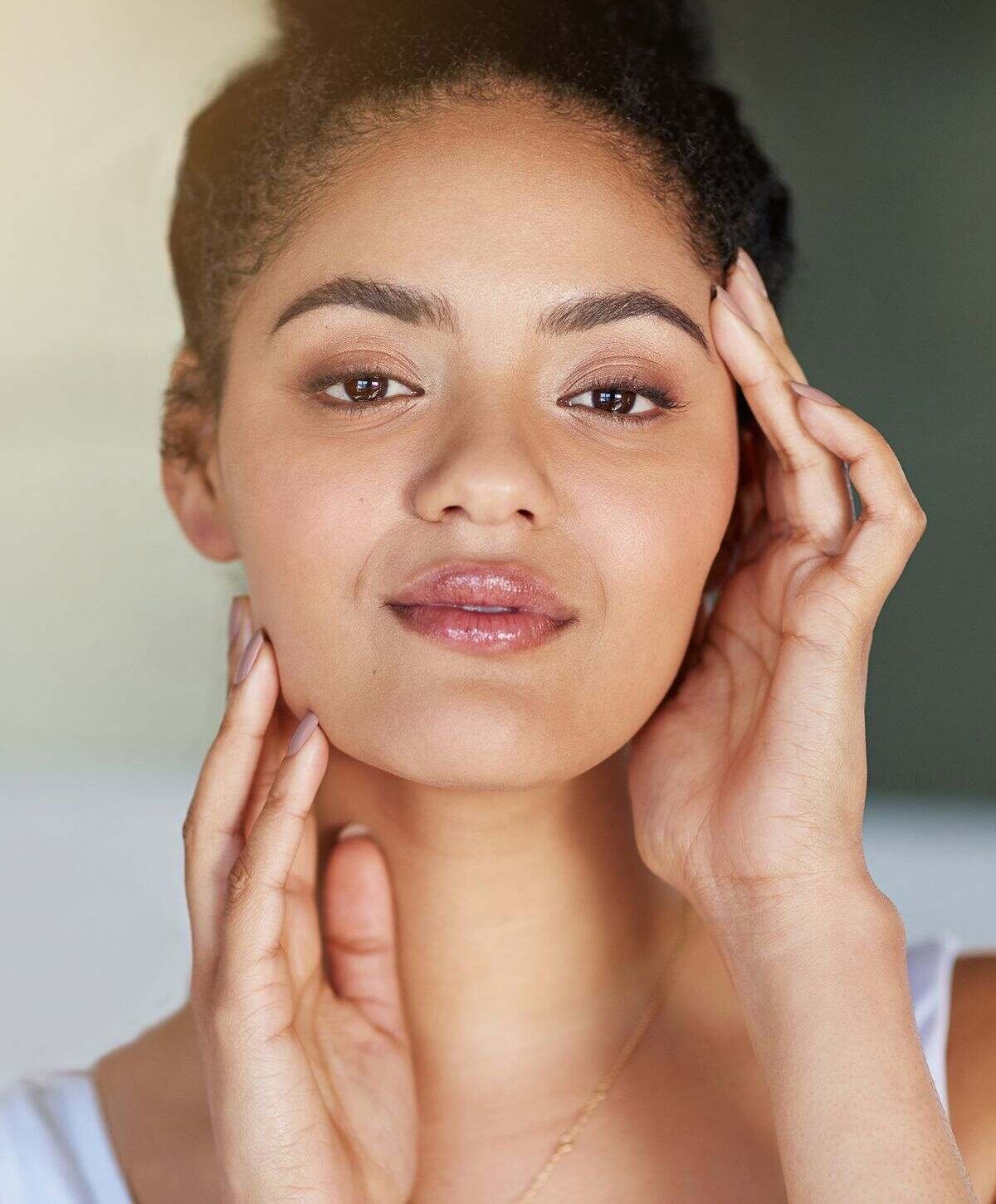 Woman gently touching her face, natural light.